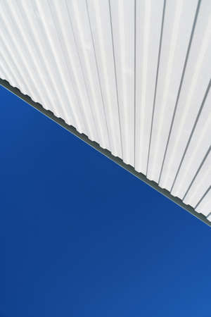 Textured white metal structures diagonally against a blue sky. Abstraction in buildingsの写真素材