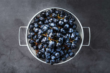 Ripe black grapes in a metal bowl on a black background. Top viewの写真素材