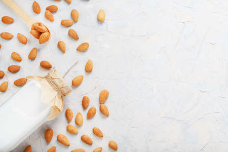 Almond milk in a glass bottle on a light background with a scattering of seed kernels and a wooden spoon. Top viewの写真素材