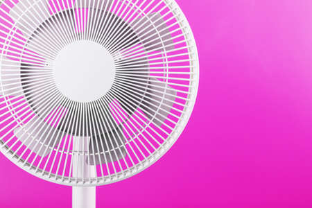 The grille and blades of the electric fan are white on a pink background.の写真素材