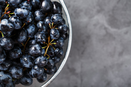 Ripe black grapes in a metal bowl on a black background. Top viewの写真素材