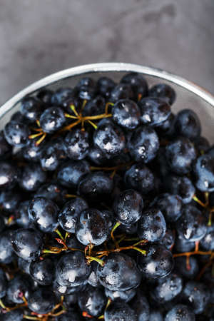 Sweet black grapes in a metal bowl on a dark textured background. Top viewの写真素材