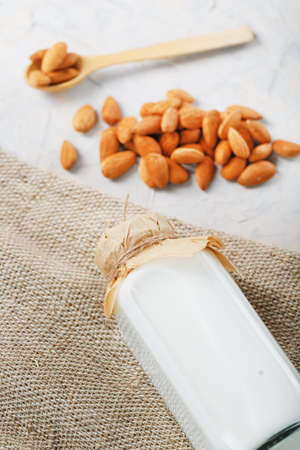 Almond milk in a bottle with a handful of grains and a wooden spoon with a burlap cloth on a light background. Top viewの写真素材