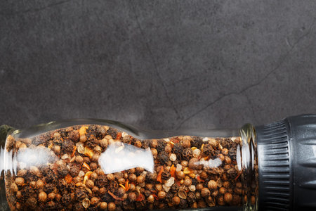 A mixture of seasonings, spices and herbs in a glass mill on a black background. Free space top...