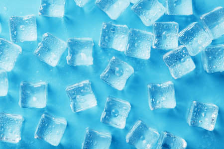 Lots of ice cubes with water drops scattered on a blue background top view