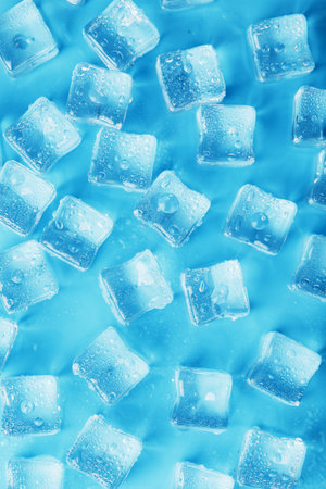 Many frosty and refreshing ice cubes with drops on a blue background. Refreshing drinks in hot...