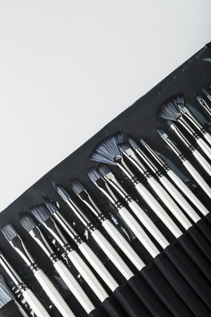 Brushes, palette knives in a pencil case on a white canvas background. top view with free spaceの写真素材