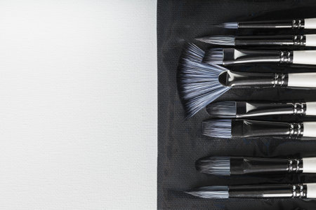 Brushes, palette knives in a pencil case on a white canvas background. top view with free spaceの写真素材