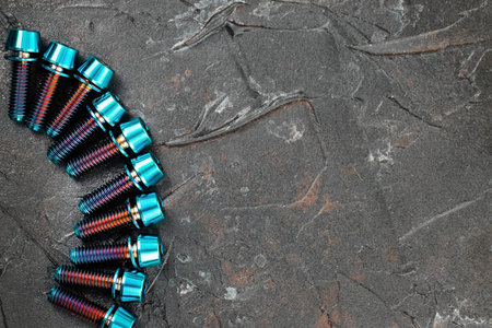 A row of blue Titanium bicycle screws on a black textured background with free space, top view