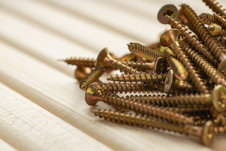 A pile of screws on a table made of wooden slats with warm lighting and free spaceの写真素材