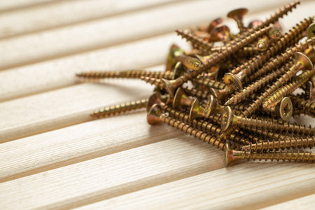 A pile of screws on a table made of wooden slats with warm lighting and free spaceの写真素材