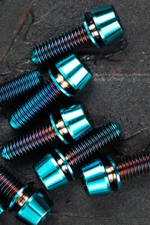 Screws made of blue-purple anodized titanium alloy on a black textured background, anodic oxide...