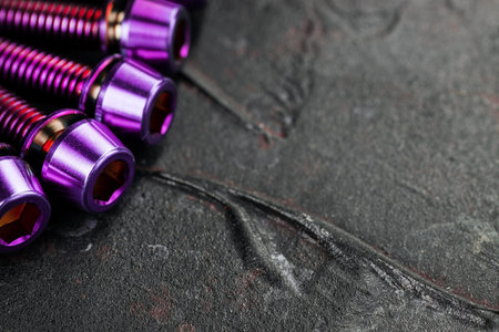 A series of purple hexagon head screws on a black textured background close-upの写真素材