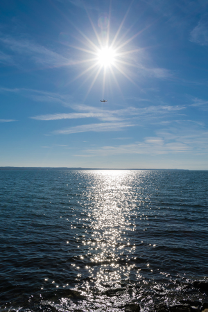 Airplane flying over sea and below the sun at Thessaloniki, Greeceの写真素材