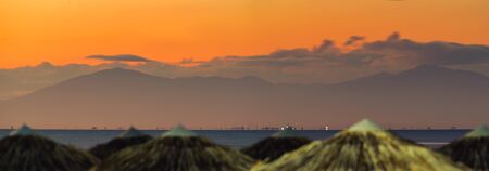 The home of the twelve Greek Gods, Mountain . The panoramic photograph was taken during sunset from Perea's beach, wicker umbrellas are visible at the foreground.の写真素材