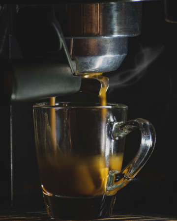 Espresso glass cup in machine, hot coffee brewingの写真素材