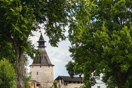 stone tower with a wooden roof of the Pskov Kremlin surrounded by trees with green foliageの写真素材