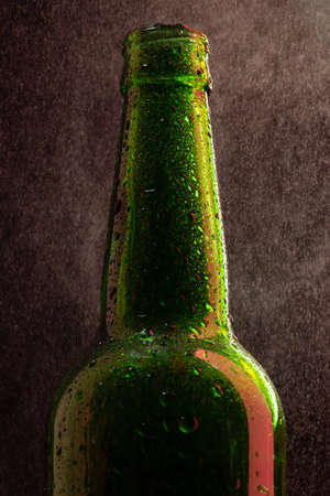 Cold beer bottle with drops and red highlight on black under spray close-upの写真素材