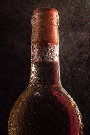 White wine bottle with drops and red highlight under spray on black backgroundの写真素材