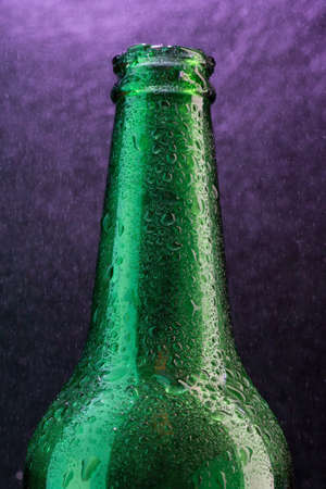 Cold beer bottle with drops on violet under spray close-upの写真素材