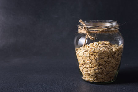 useful tasty oatmeal in a transparent glass jar on a dark background
