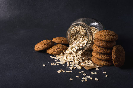 useful tasty oatmeal in a transparent glass jar and oatmeal cookies on a dark backgroundの写真素材