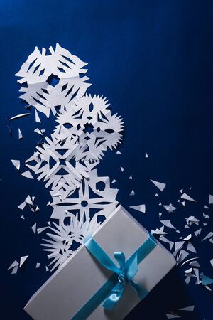 background of various Christmas themed snowflakes cut out of white paper on a trendy blue background 2020 with a giftの写真素材