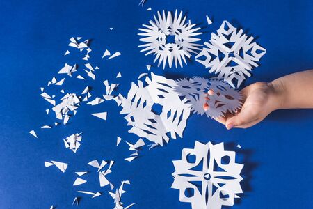background of various Christmas themed snowflakes cut out of white paper on a trendy blue background 2020 with a giftの写真素材