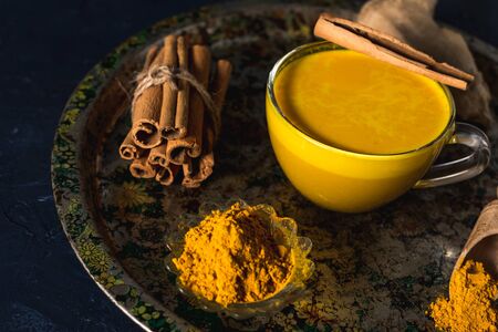 Golden turmeric milk on the dark background with spices cinnamon and ingredientsの写真素材