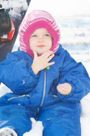 Baby sitting on the snow in front of a snowboardの写真素材