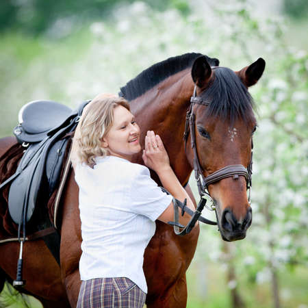 Woman and bay horse in apple garden. Portrait of horse and beautiful lady. Horse rider. Equestrian sport.の写真素材