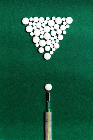 pool game with white pills and thermometer on green felt background, flat lay concept