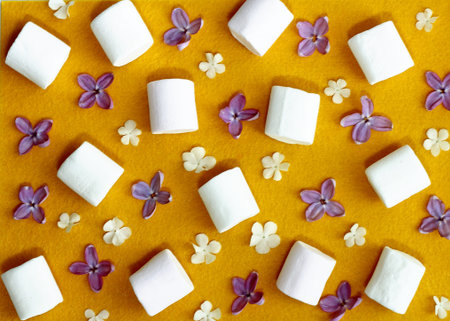 pattern with lilac flowers and white marshmellow on yellow felt background. flat ley. top view.