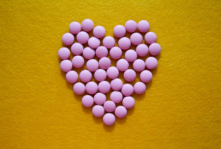 heart made of pink pills on bright yellow felt background. medical or Valentine's day conceptの写真素材