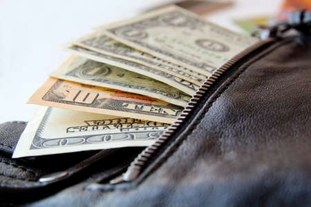 dollar bills peeking out of the black leather bag, close-upの写真素材