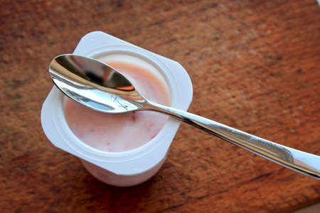 Strawberry pink yogurt in white plastic cup on a wooden rustic background with spoon on it.の写真素材