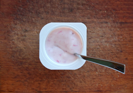 Pink strawberry yogurt in white plastic cup on a wooden rustic background with spoon on it. Top view, flat lay.の写真素材