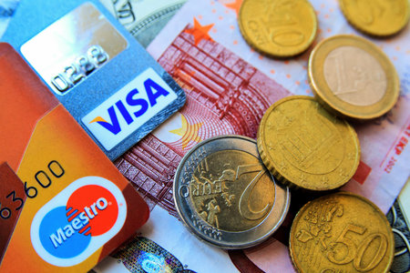 stack of multicolored credit cards by Visa and Maestro and euro bills and coins scattered around, close-up. Illustrative editorial.のeditorial素材