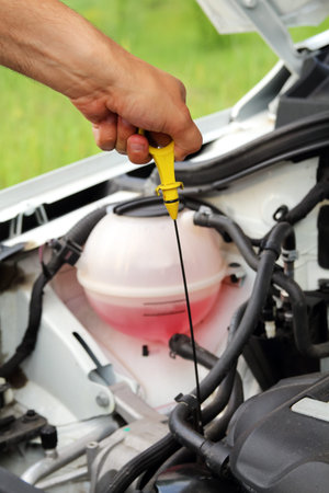 Mechanic checking oil level in a car workshop: male hand with dipstick close-up.