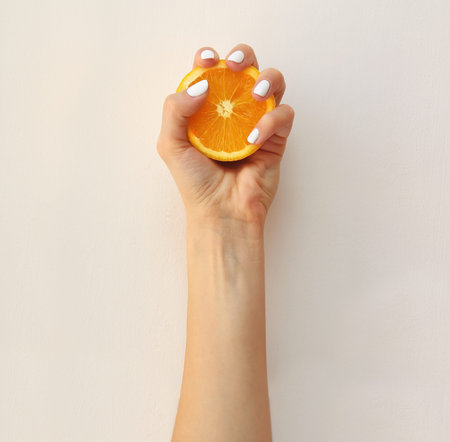 A female hand squeezing half an orange. Vitamin C concept in minimal style.の写真素材