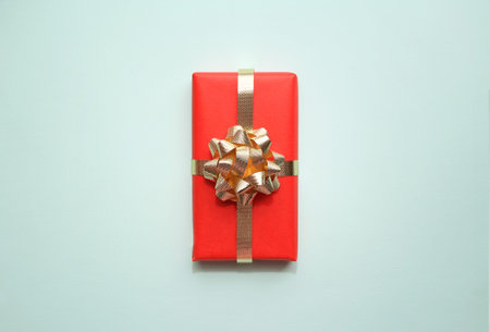 Red gift box with golden ribbon on soft blue background with copy space. Christmas or Birthday...