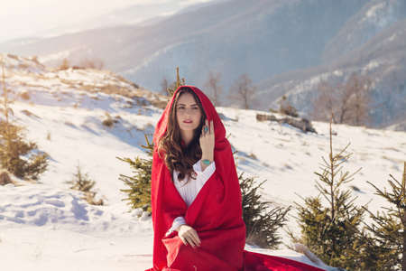 Young woman in red riding hood costume, on a snowy mountain backgroundの写真素材