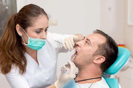 Dentist giving an injection of anesthesia to the patient. Young man at the dental clinicの写真素材