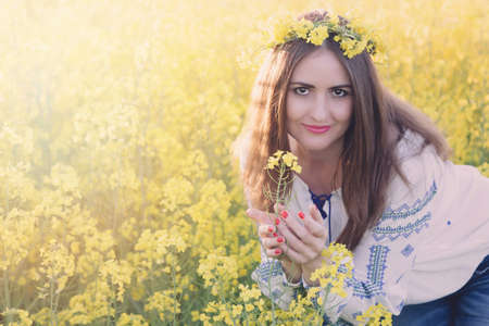 Portrait of a young woman in a rapeseed field. Young joyful girl wearing traditional romanian blouseの写真素材