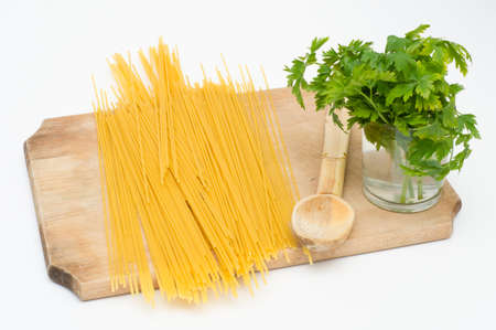 Spagetti on a wooden board with a spoon and some green spicesの写真素材