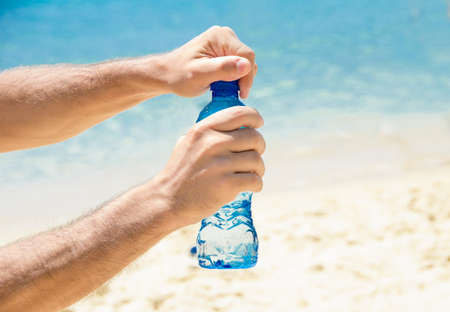 Two hands openning a bottle on a hot summer day at the beachの写真素材
