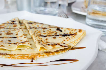 Pancakes with chocolate syrup on white plate with white clothの写真素材