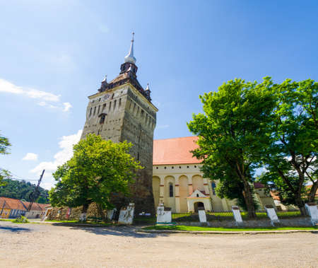 Fortified medieval Evanghelic Church in Saschiz, Mures County, Transylvania Region of Romania built in a gothic style with a large stone bell and clock towerの写真素材