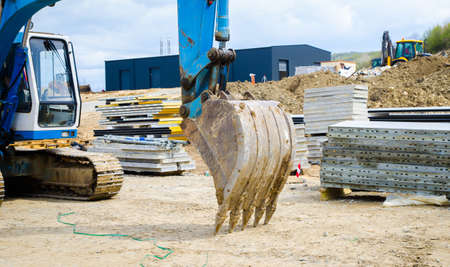 Bucket on a blue excavator standing still on a construction site with diggers building and framing on the background suggesting construction wor and engineeringの写真素材