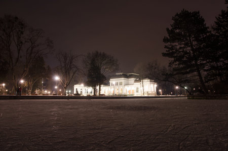 Cluj Napoca casino in central park on a cold snowy winter night in a scene taken from the frozen lake where people skate with bright lightsの写真素材